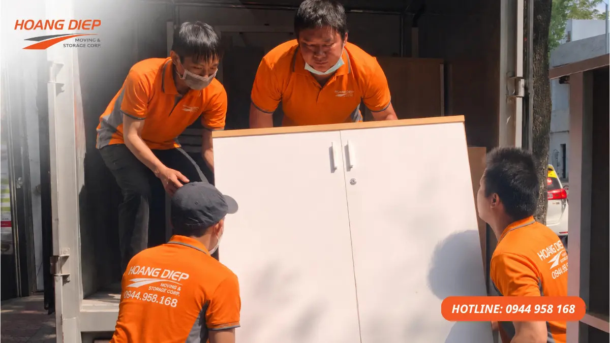 Hình ảnh nhân viên Nâng Hạ & Vận Tải Hoàng Diệp phối hợp bốc xếp tủ gỗ lên xe tải, minh họa công đoạn bốc xếp và vận chuyển tài sản trong quy trình chuyển nhà trọn gói.